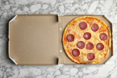 Tasty pepperoni pizza in cardboard box on white marble table, top view
