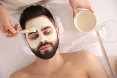Photo of Cosmetologist applying mask on man's face in spa salon, top view
