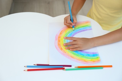 Little child drawing rainbow at white table, closeup. Stay at home concept