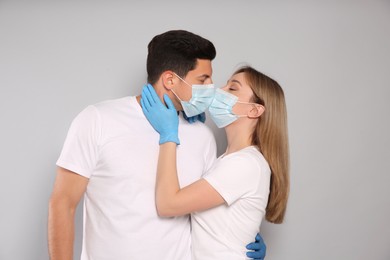 Couple in medical masks and gloves trying to kiss on light background