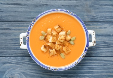 Tasty creamy pumpkin soup with croutons and seeds in bowl on blue wooden table, top view