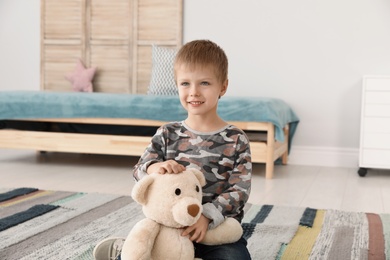 Cute little boy playing with teddy bear at home