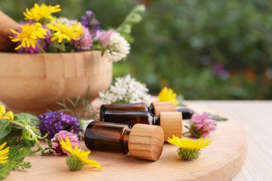 Bottles of essential oil, flowers and herbs on white wooden table, closeup. Space for text