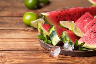Slices of delicious ripe watermelon, ice cubes and cut lime on wooden table, space for text
