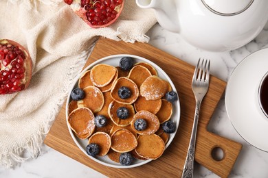 Delicious mini pancakes cereal with blueberries served on white marble table, flat lay