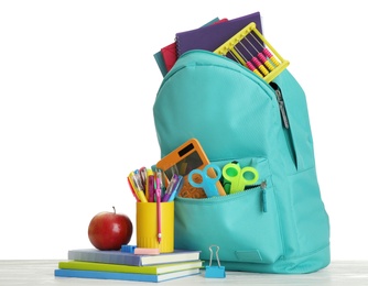 Stylish backpack with different school stationary and apple on wooden table against white background