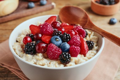 Bowl with tasty oatmeal porridge and berries served on wooden table, closeup. Healthy meal