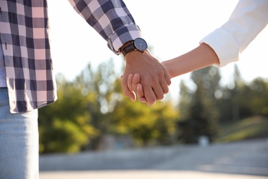 Couple holding hands together outdoors on summer day, closeup