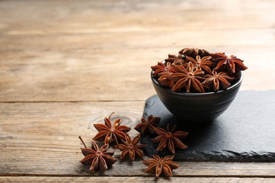 Photo of Aromatic anise stars with bowl on wooden table. Space for text