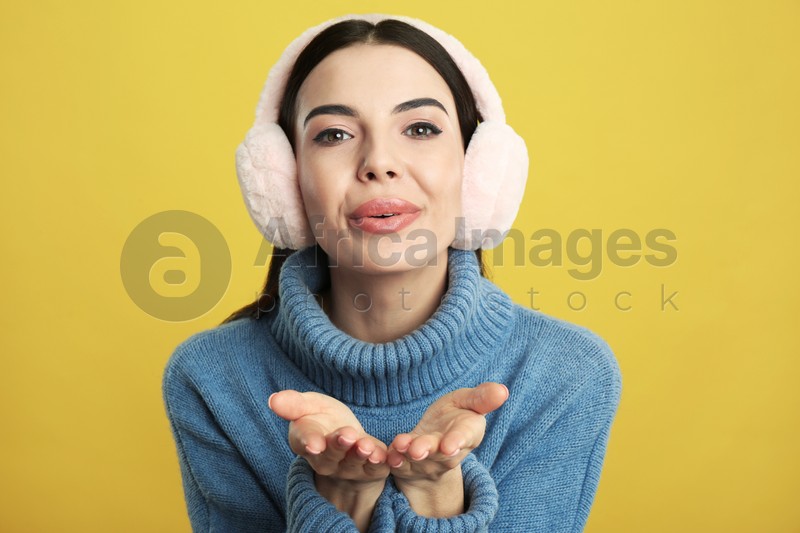 Beautiful young woman wearing earmuffs on yellow background
