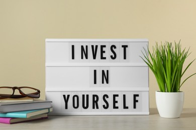 Lightbox with motivational quote Invest in Yourself, stationery and plant on white wooden table