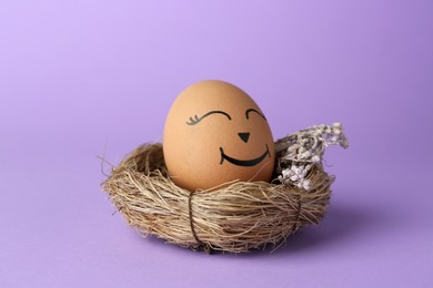 Egg with drawn happy face in nest on lilac background, closeup