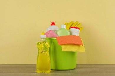 Bucket with different cleaning supplies on wooden floor near beige wall