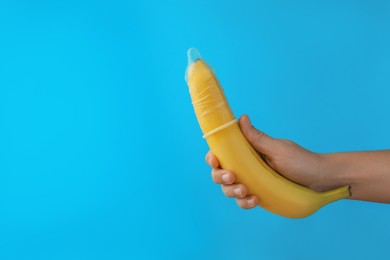 Woman holding banana in condom on light blue background, closeup and space for text. Safe sex concept
