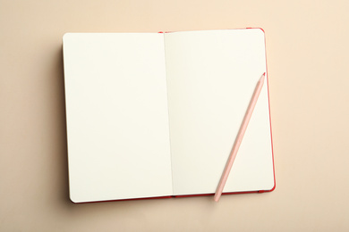 Stylish open notebook and pencil on beige background, top view