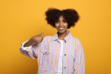 Photo of Smiling African American woman showing thumbs up on orange background
