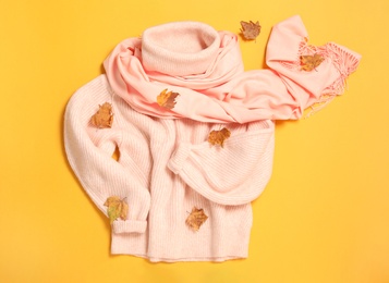 Pink sweater, scarf and dry leaves on yellow background, flat lay. Autumn season