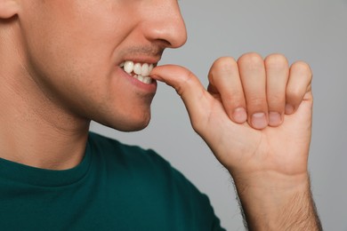Man biting his nails on grey background, closeup. Bad habit