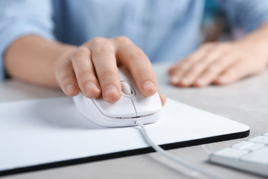 Woman using wired computer mouse on pad at light grey marble table, closeup