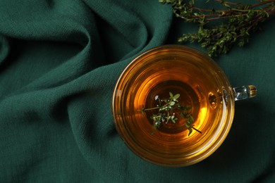 Photo of Glass cup of aromatic herbal tea with thyme on green fabric, top view. Space for text