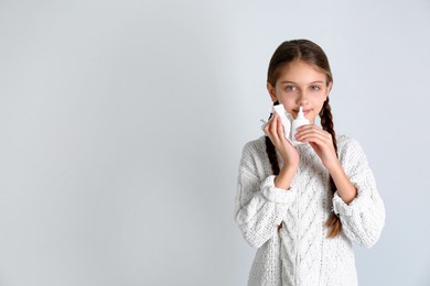 Sick little girl using nasal spray on white background. Space for text