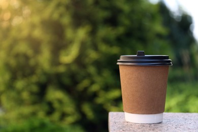 Photo of Disposable paper cup with plastic lid on stone parapet outdoors, space for text