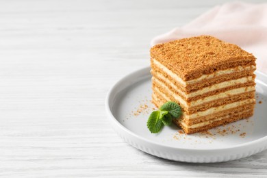 Slice of delicious layered honey cake with mint served on white wooden table. Space for text