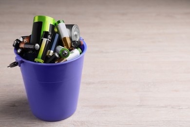 Image of Used batteries in bucket on white wooden table, space for text