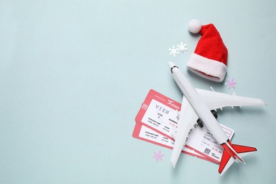 Santa hat, toy airplane and airline tickets on light blue background, space for text. Christmas vacation