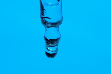 Dripping face serum from pipette on blue background, closeup