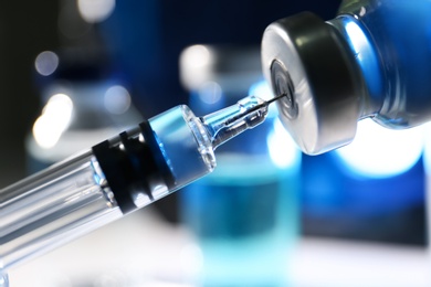 Filling syringe with vaccine from vial on blurred background, closeup