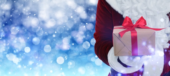 Image of Santa Claus holding gift box on winter background, bokeh effect. Space for text