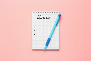 Notebook with goal list and pen on pink background, top view