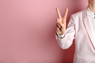 Young woman showing victory gesture on color background. Space for text
