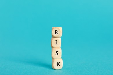 Word Risk made of small wooden cubes on turquoise background