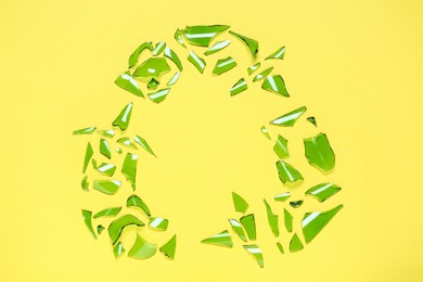 Photo of Recycling symbol made of glass pieces on yellow background, flat lay