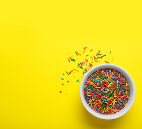 Colorful sprinkles in bowl on yellow background, top view with space for text. Confectionery decor