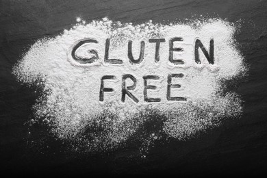 Phrase Gluten free written with flour on black table, top view