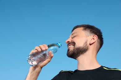 Photo of Happy man drinking water against blue sky on hot summer day. Refreshing drink