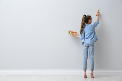 Little girl painting on light wall indoors, back view. Space for text
