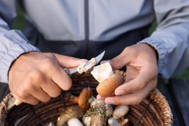 Man peeling mushroom with knife over basket, closeup