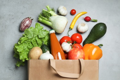 Overturned paper bag with bottle of juice, vegetables and fruits on grey background, flat lay