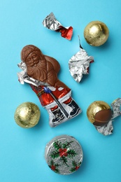 Chocolate Santa Claus and sweets on light blue background, flat lay