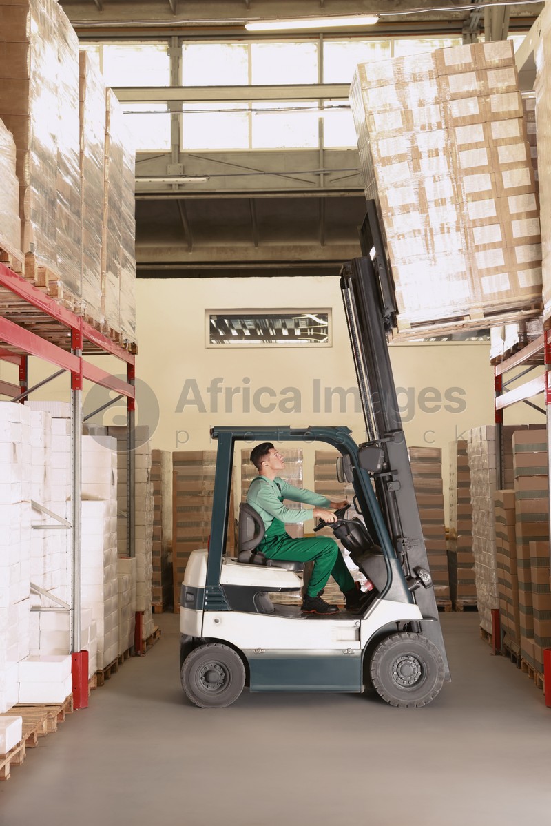 Worker sorting cardboard boxes with forklift truck in warehouse. Logistics concept