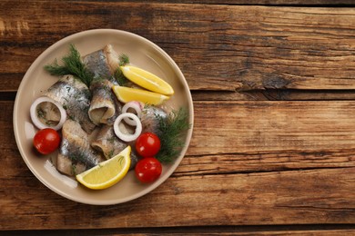 Photo of Salted herring fillets served with lemon, cherry tomatoes and onion on wooden table, top view. Space for text