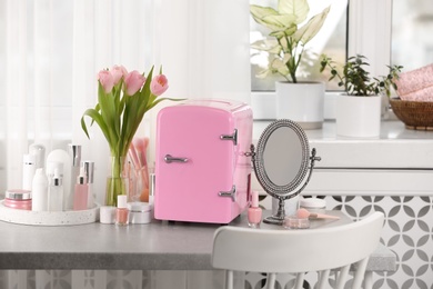Pink mini cosmetics refrigerator and skin care products on table