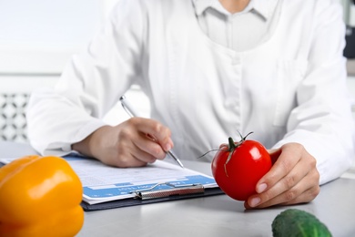 Scientist with laboratory test form and fresh tomato at table indoors, closeup. Poison detection