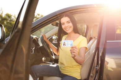 Photo of Happy young woman holding license while sitting in car outdoors. Driving school