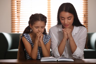 Young woman with her little daughter praying together over Bible at home