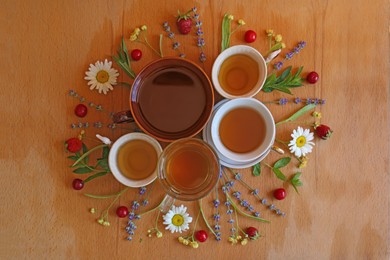 Cups with tasty herbal tea, different flowers and fruits on wooden table, flat lay